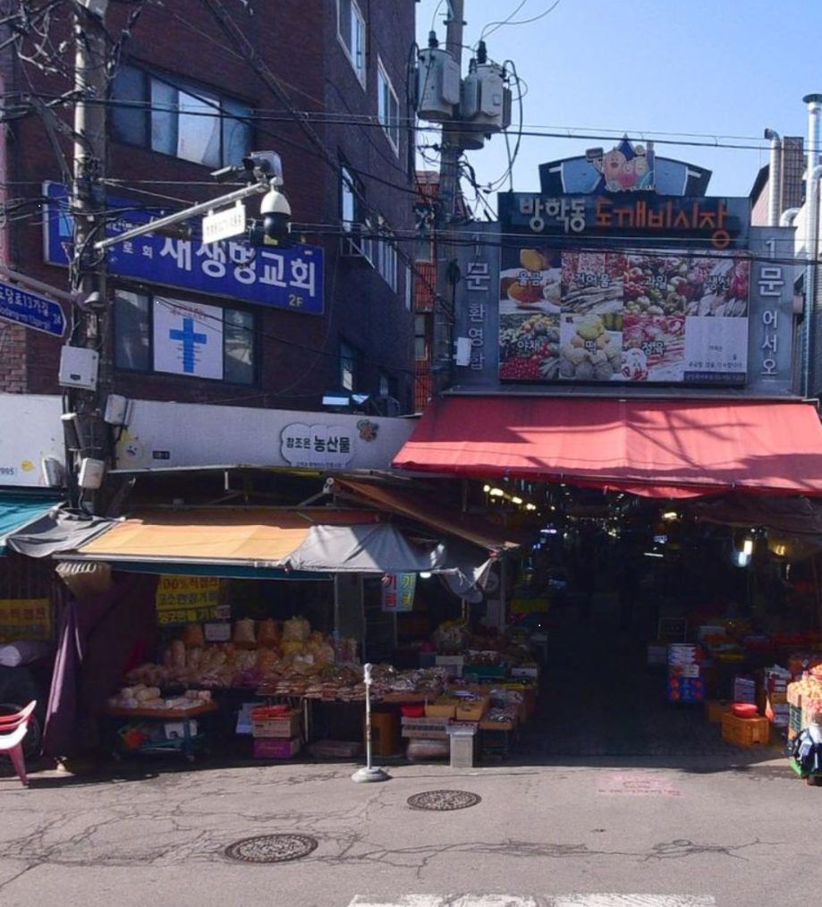 방학동 도깨비시장 1문 입구. 붉은 차양 위로 시장 간판이 걸려 있고 왼쪽에 참조은 농산물 간판이 보인다.